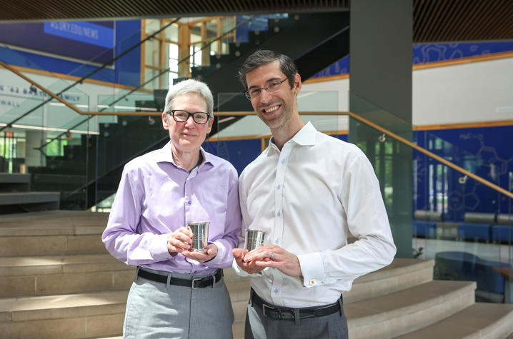 two people pose with their mint julet cup award statuettes in front of an atrium