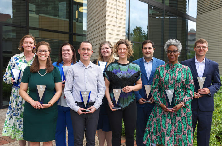 nine people stand holding statuettes in front of an academic building