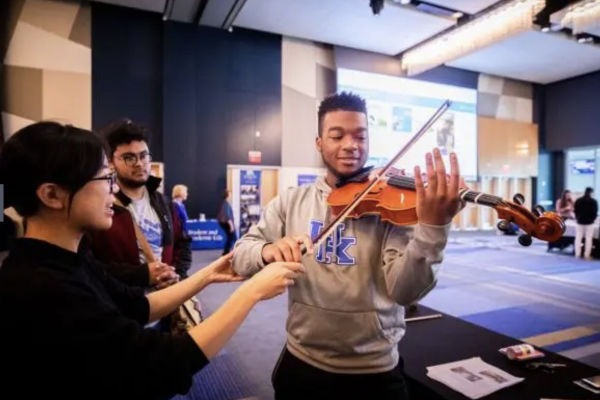 a student participant plays a violin guided by the experts staffing a booth at the curiosity fair