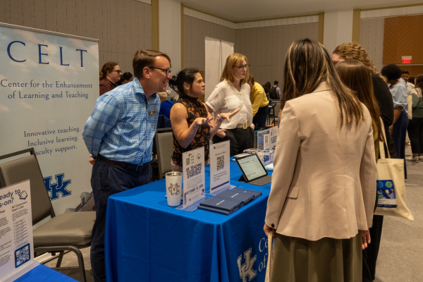 three people stand behind a blue-draped table with a CELT sign behind it, speaking to three new faculty about CELT