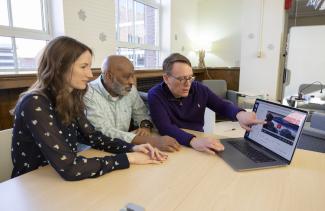 three people sitting at a table examining a laptop screen in 502 king library