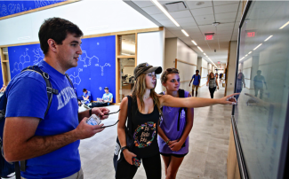 Students looking at a video screen while one points at it.
