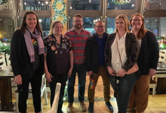 six celt staff standing and smiling in a brightly lit restaurant with holiday decorations