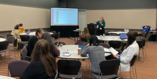 celt staff Jennifer Pusateri and Mike Wallace speaking in front of several round tables with POD Network conference participants