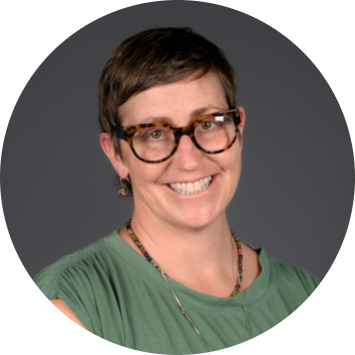 a woman with short brown hair and glasses, wearing a green shirt, smiles