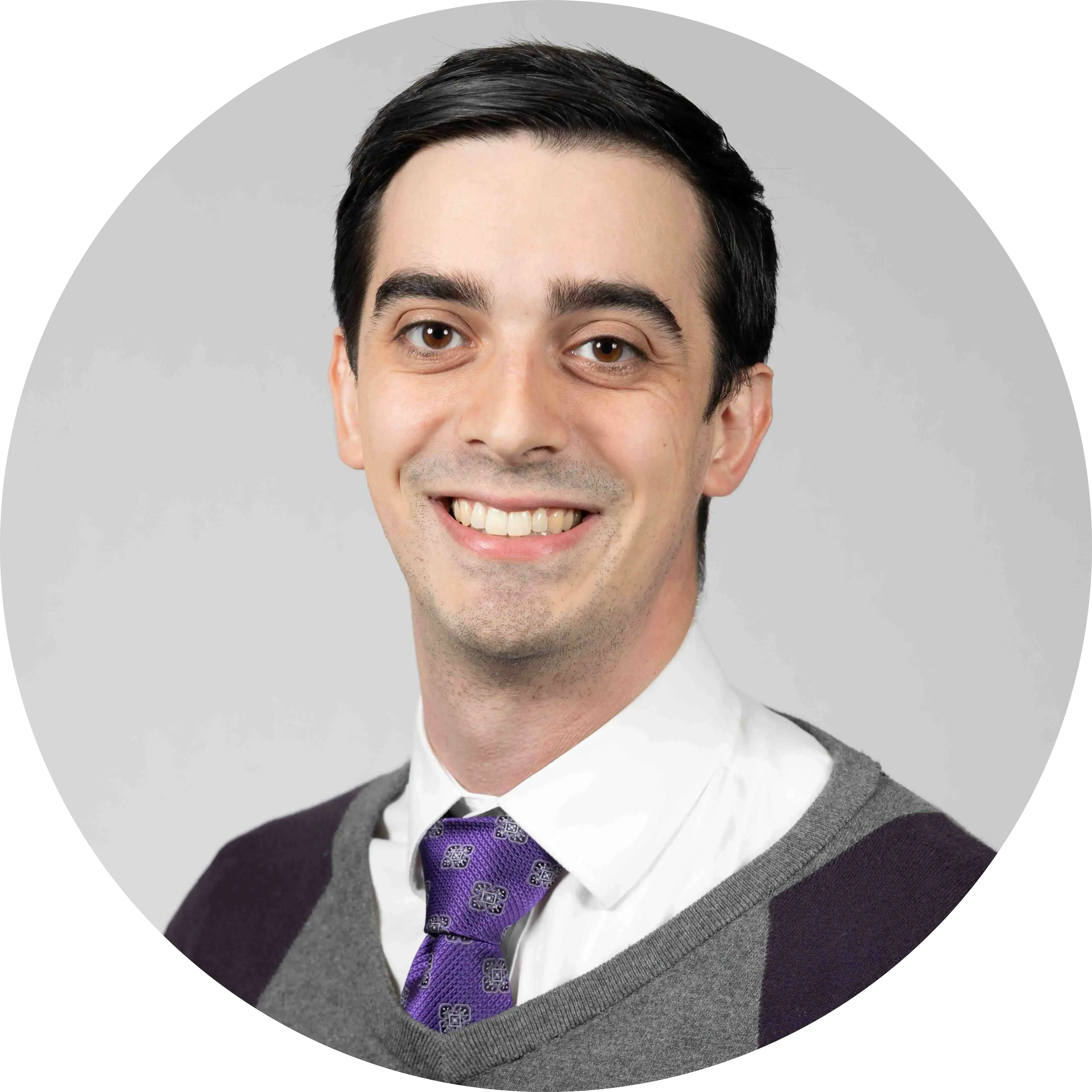 a man with short black hair smiling while wearing a white shirt and purple tie under a black and gray sweater vest